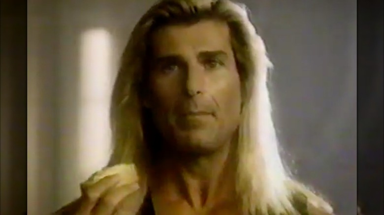 Fabio stands in a pile of rubble, wearing a leather vest, and holding buttered bread.