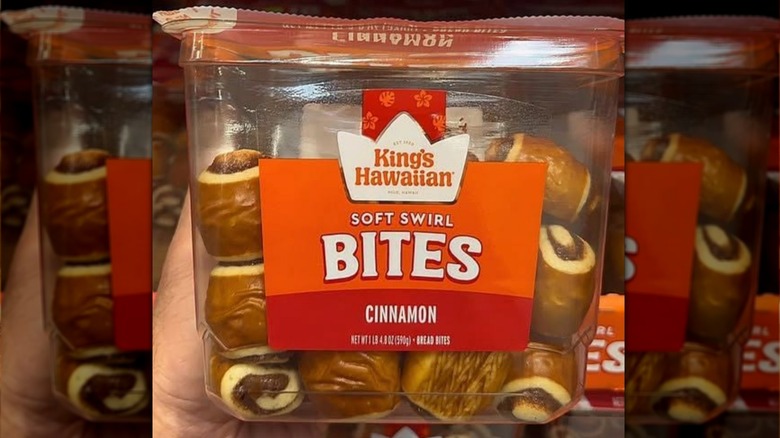 A person dipping a King's Hawaiian Cinnamon Soft Swirl Bite into a bowl of icing