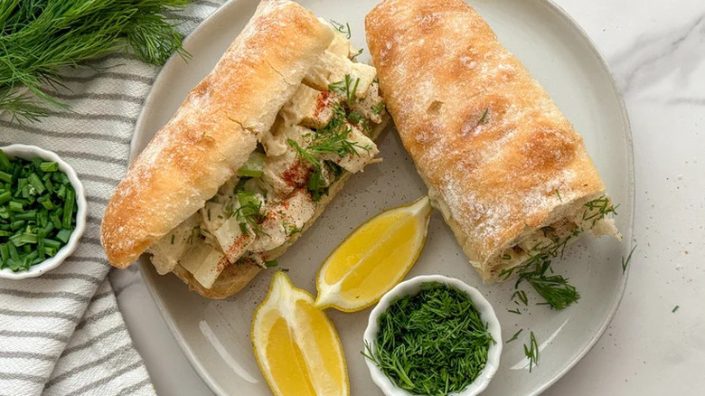 Two vegan heart of palm lobster rolls on plate with lemon wedges and fresh green herbs