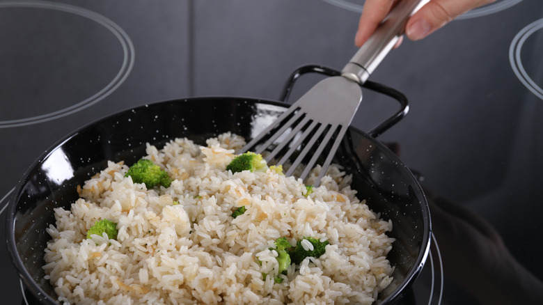Hand stirring fried rice in a pan that's cooking on an induction stovetop
