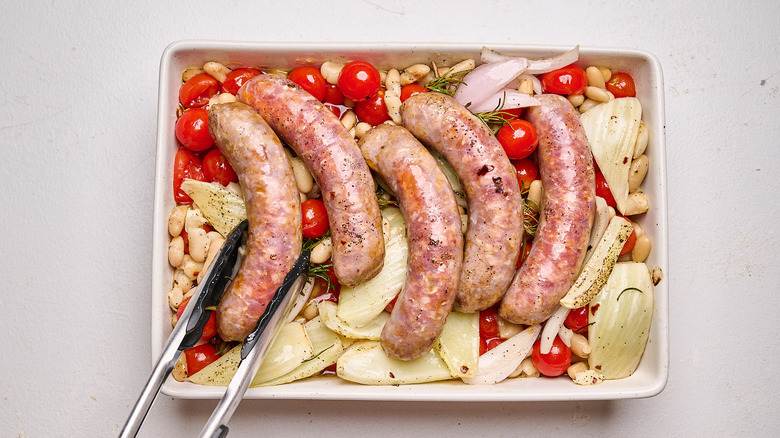 flipping roasted sausages in a dish with roasted tomatoes