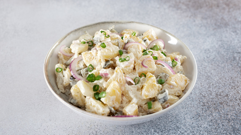 A bowl of potato salad with chives and red onion in a gray bowl on a speckled countertop