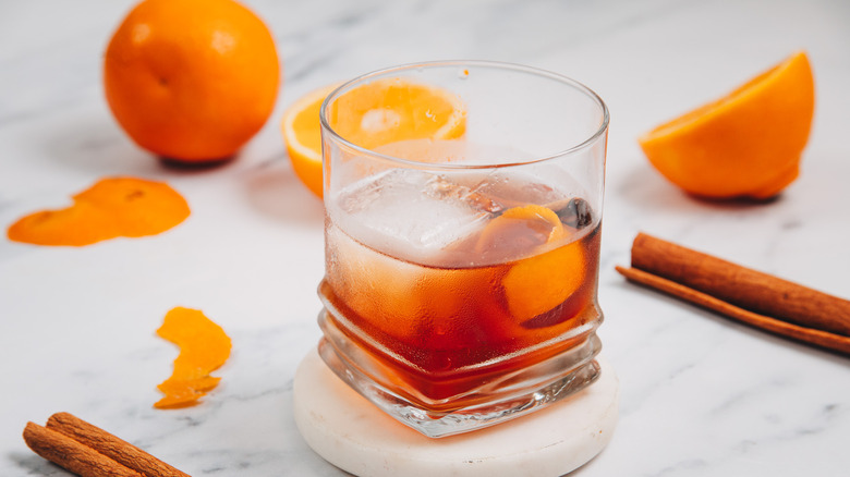 A glass of a brown butter old fashioned with oranges in background