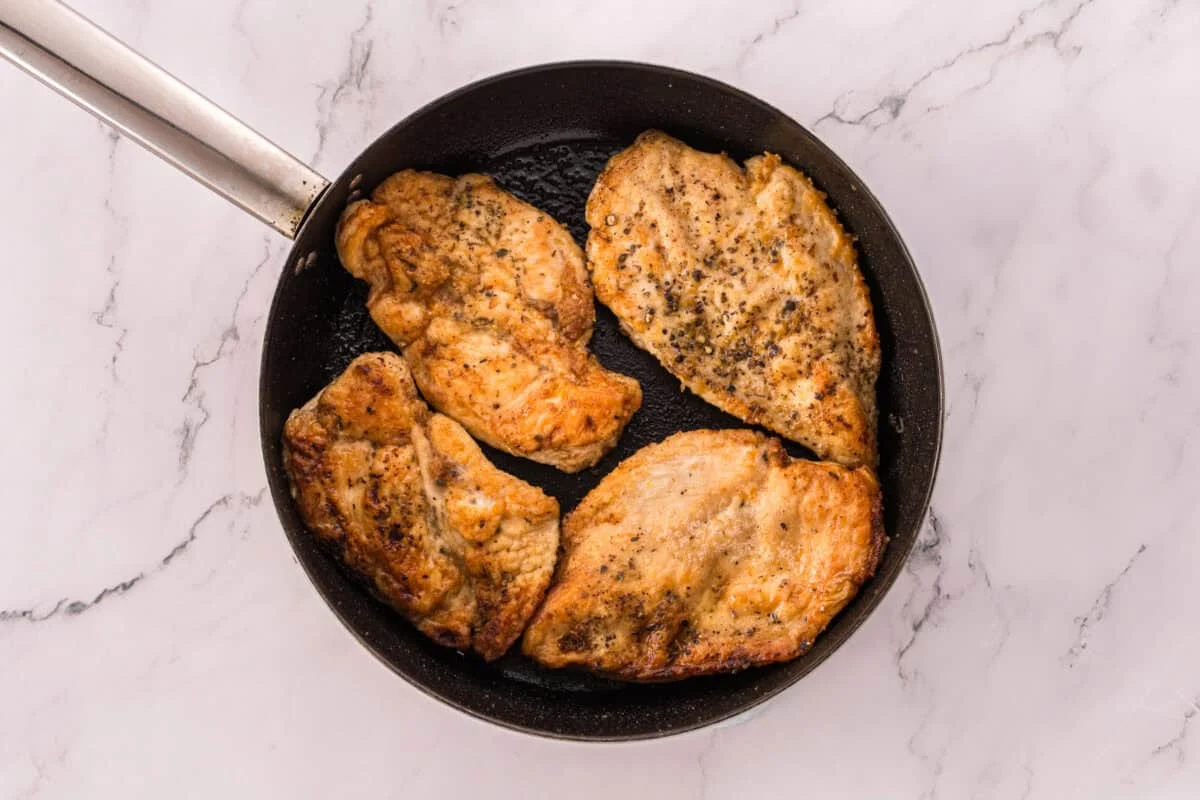 Four golden brown seared chicken breasts in a black skillet.
