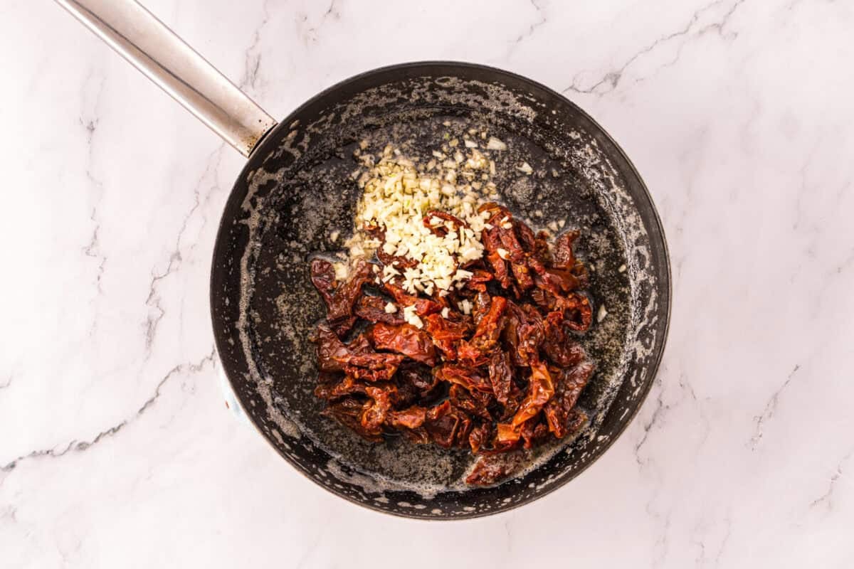 Minced garlic and sun-dried tomatoes cooking in melted butter in a skillet.