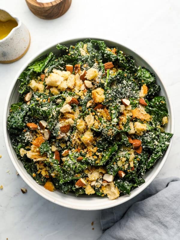 Overhead shot of kale salad in a white bowl topped with homemade breadcrumbs, chopped almonds, and grated parmesan cheese.