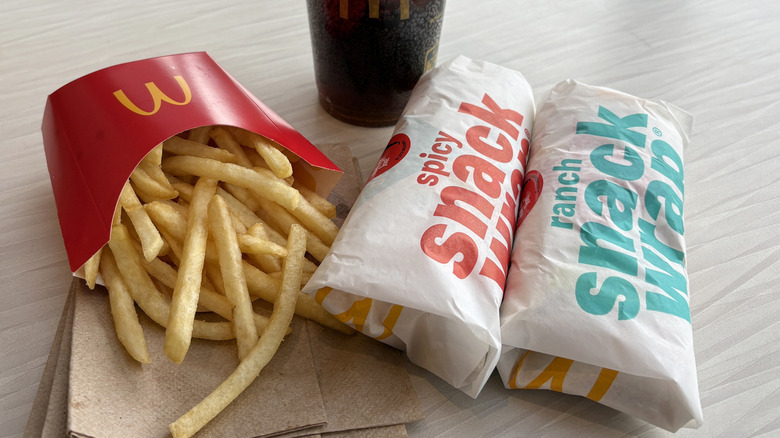 Two snack wraps sit next to a box of McDonald's Fries and a coca cola on a table. The fries are lying on a pile of napkins