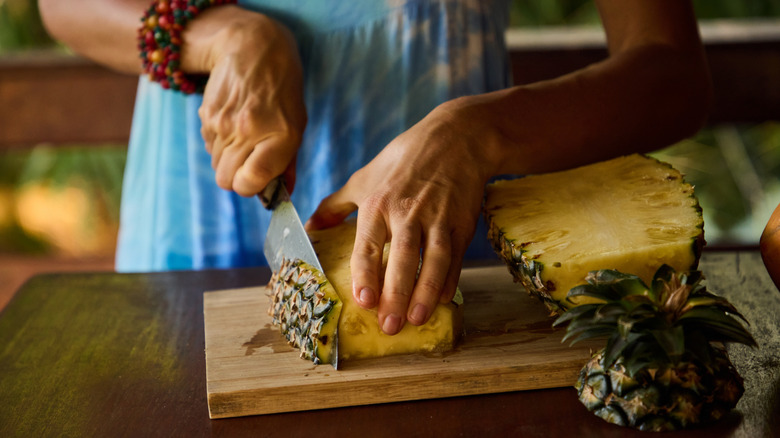Person cutting a pineapple on a cutting board