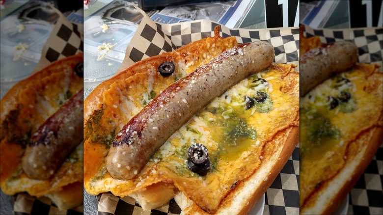 Long hot dog inside open bun with melted cheese and black olives