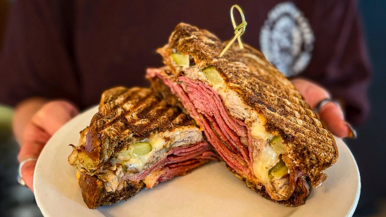 Hands holding a pastrami sandwich on a plate