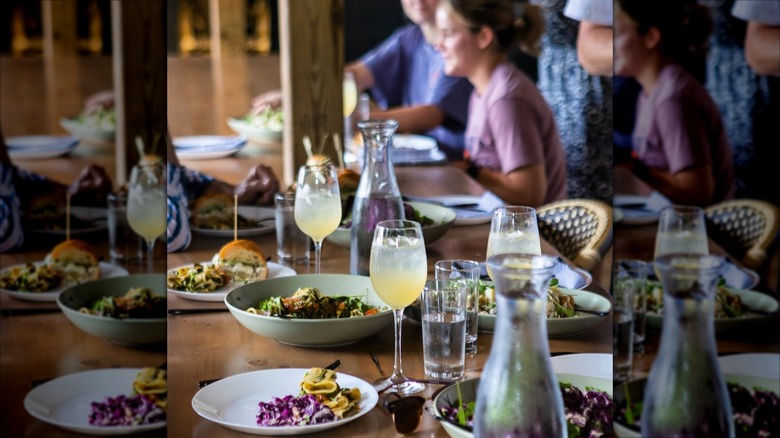 Table with many assorted dishes and cocktails with people in the background