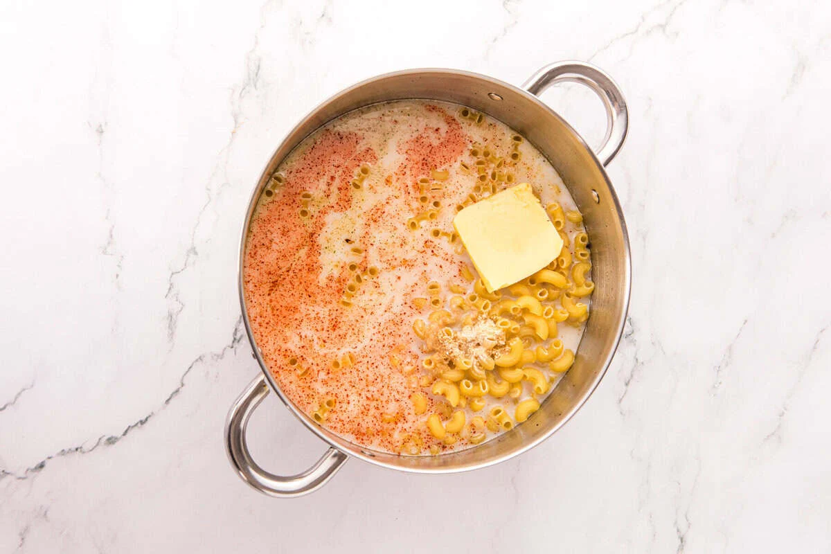 Dry elbow macaroni, chicken broth, milk, butter, and seasonings in a stainless steel pot before cooking.