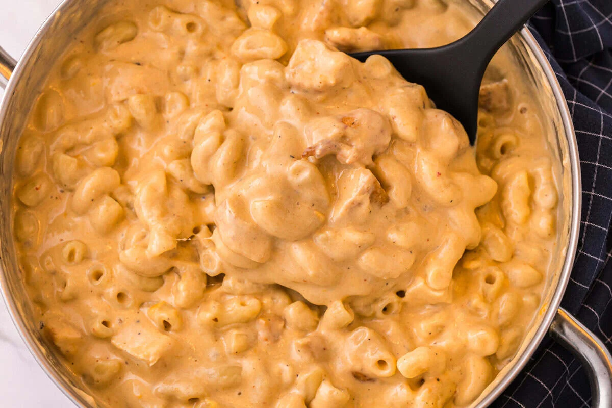 Close-up of a spatula scooping creamy buffalo chicken mac and cheese from the pot.
