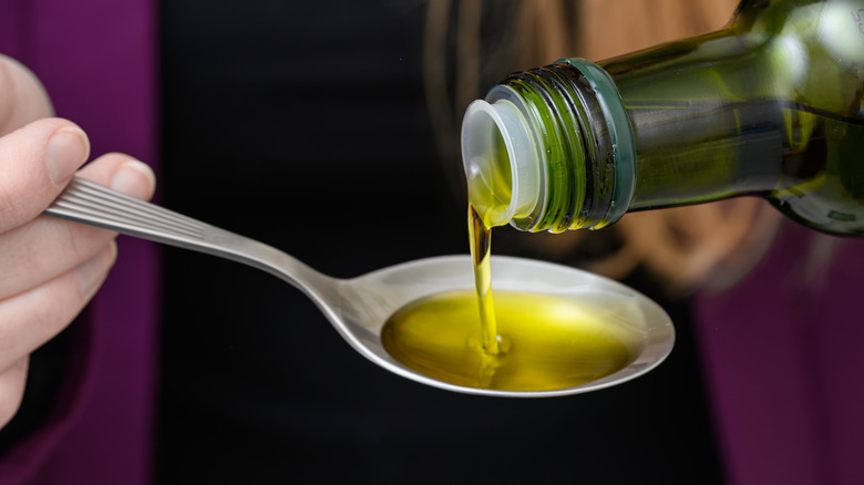 Pouring olive oil from bottle onto spoon