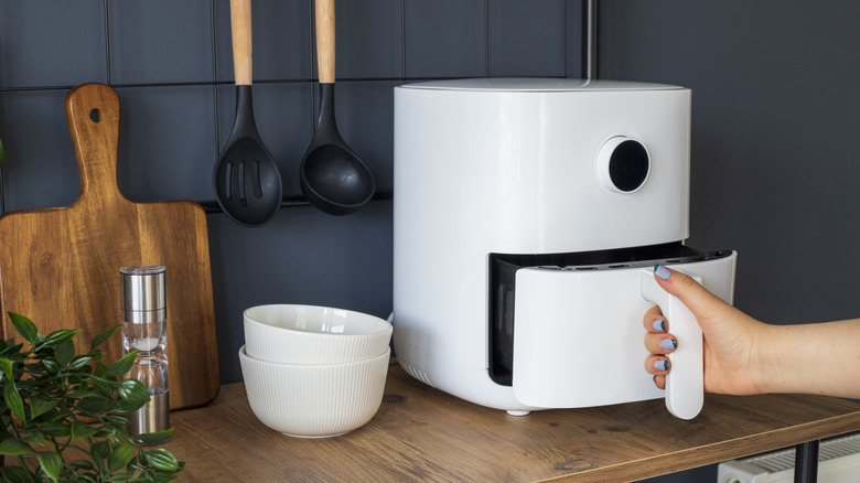 White air fryer on kitchen countertop with hand opening drawer