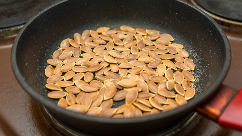 Pumpkin seeds toasting in skillet with some salt sprinkled