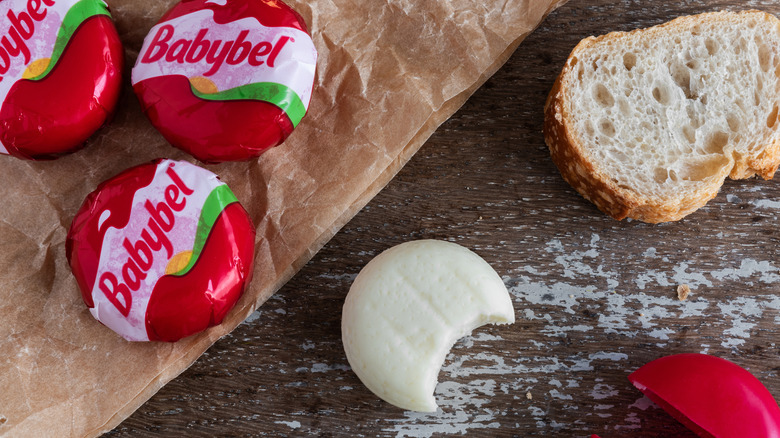 Babybel on a rustic wooden counter beside a baguette slice.
