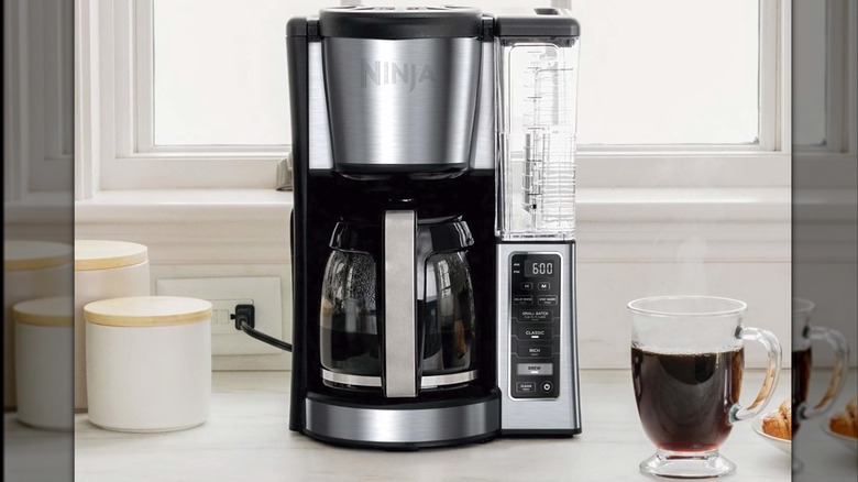 The Ninja Drip coffee maker in a white kitchen next to a glass cup