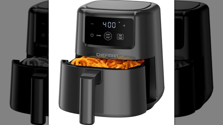 A black mini air fryer with onion rings and fries inside the basket on a white background