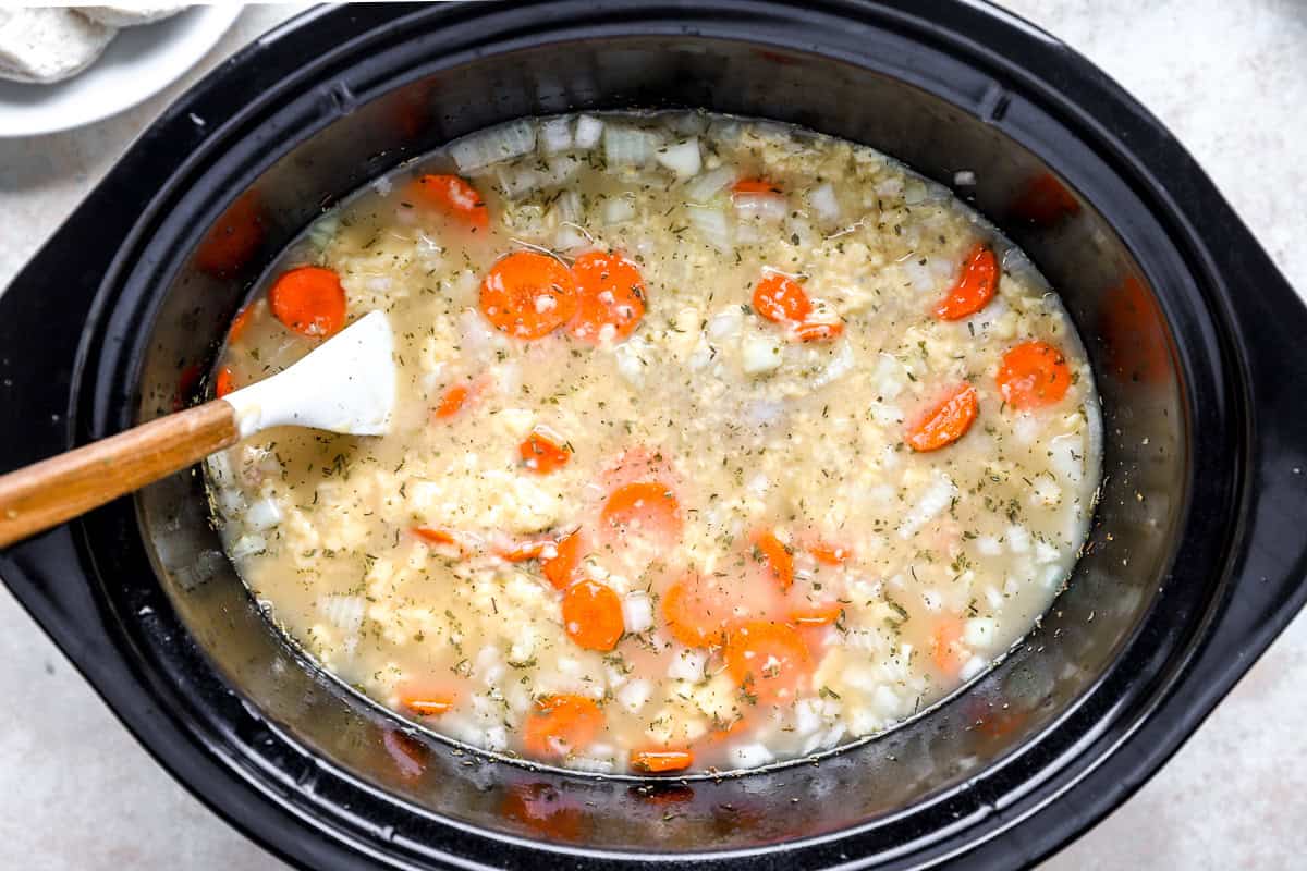 Chicken broth, sliced carrots, chopped onion, dried herbs, and cream of chicken soup in a crockpot before cooking.