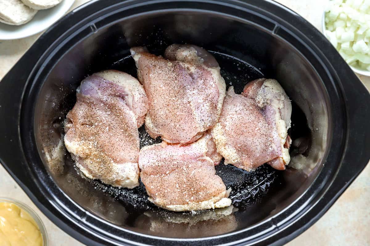 Boneless, skinless chicken thighs seasoned with salt and pepper in the bottom of a slow cooker.