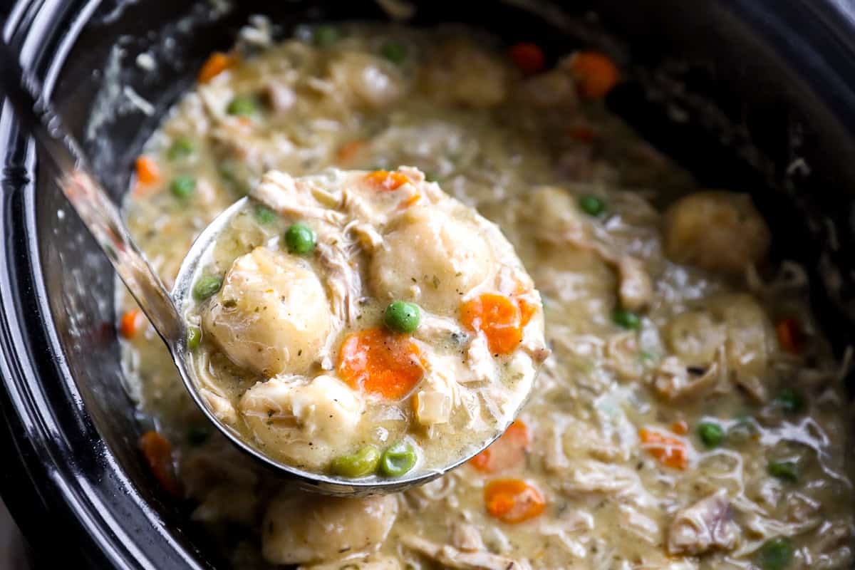 Spoon lifting a biscuit dumpling from a bowl of chicken and dumplings to show its fluffy, cooked-through center.