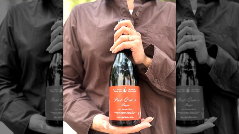 A woman in a brown shirt holds bottle of Filipa Pato Post Quercus Baga Bairrada.