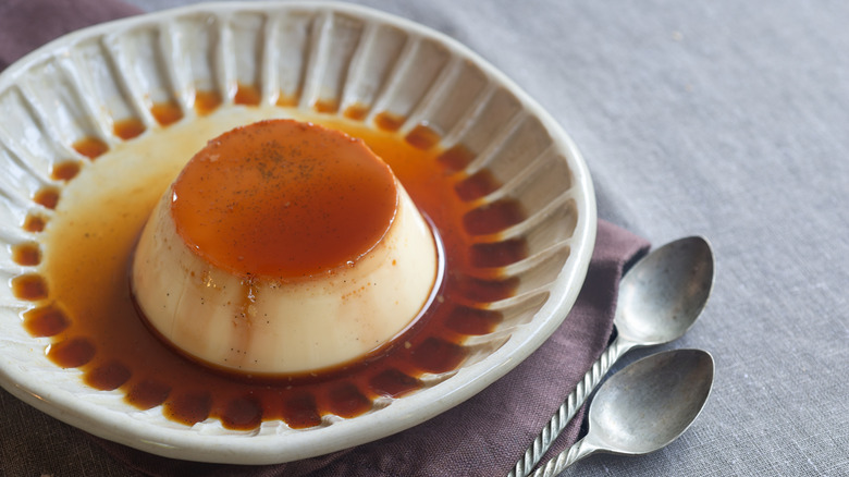 Creme caramel in a cermaic plate with two dessert spoons next to it