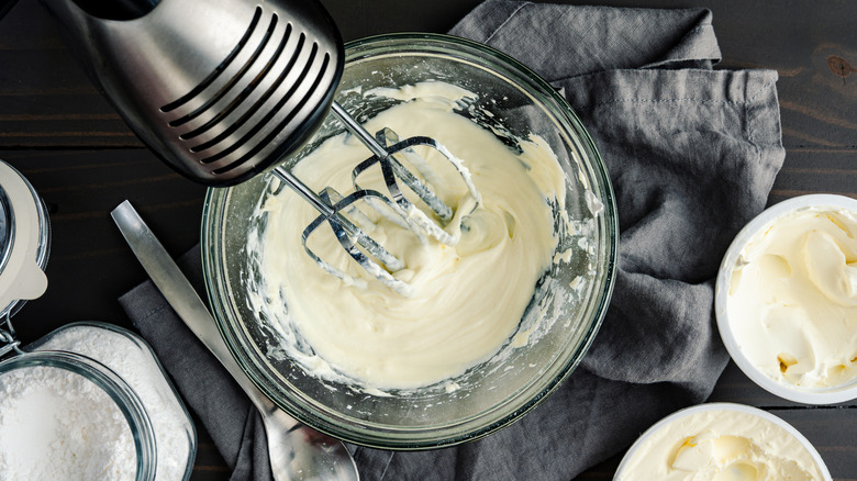 A hand mixer in a bowl with powdered sugar and cream cheese