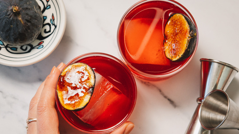 Serving two cocktails with jiggers and whole fig