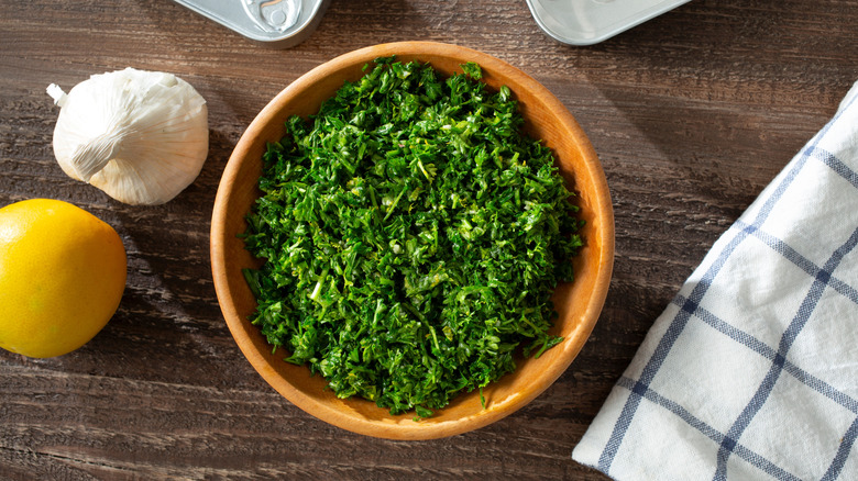 ingredients for gremolata, including parsley chopped in a bowl, garlic and lemon