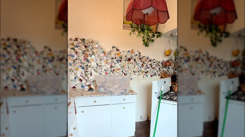 Mosaic on kitchen wall with a bucket of broken dish pieces on a counter.