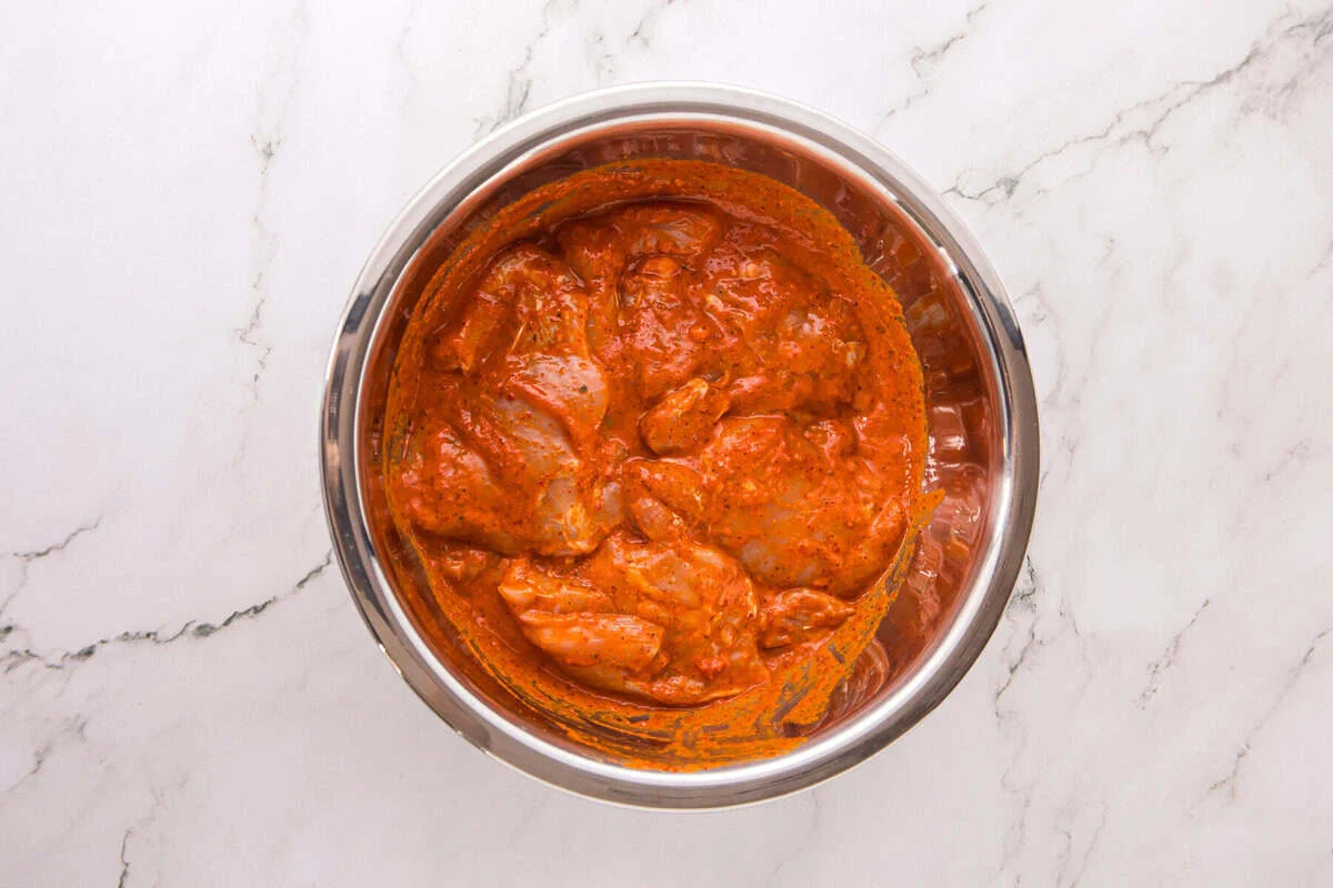 Boneless chicken thighs coated in peri peri marinade in a stainless steel bowl.