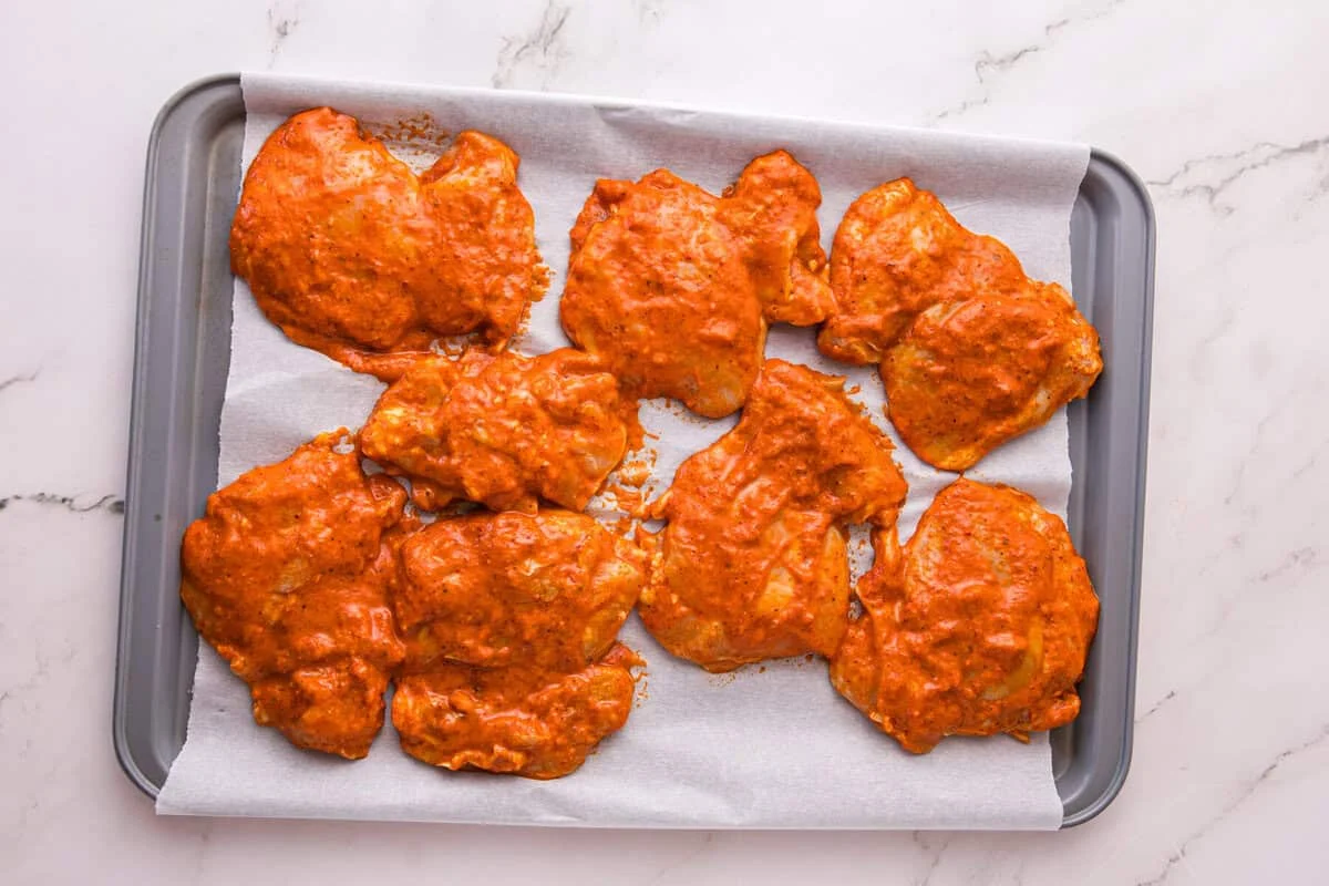 Marinated chicken thighs spaced apart on a parchment-lined sheet pan before baking.