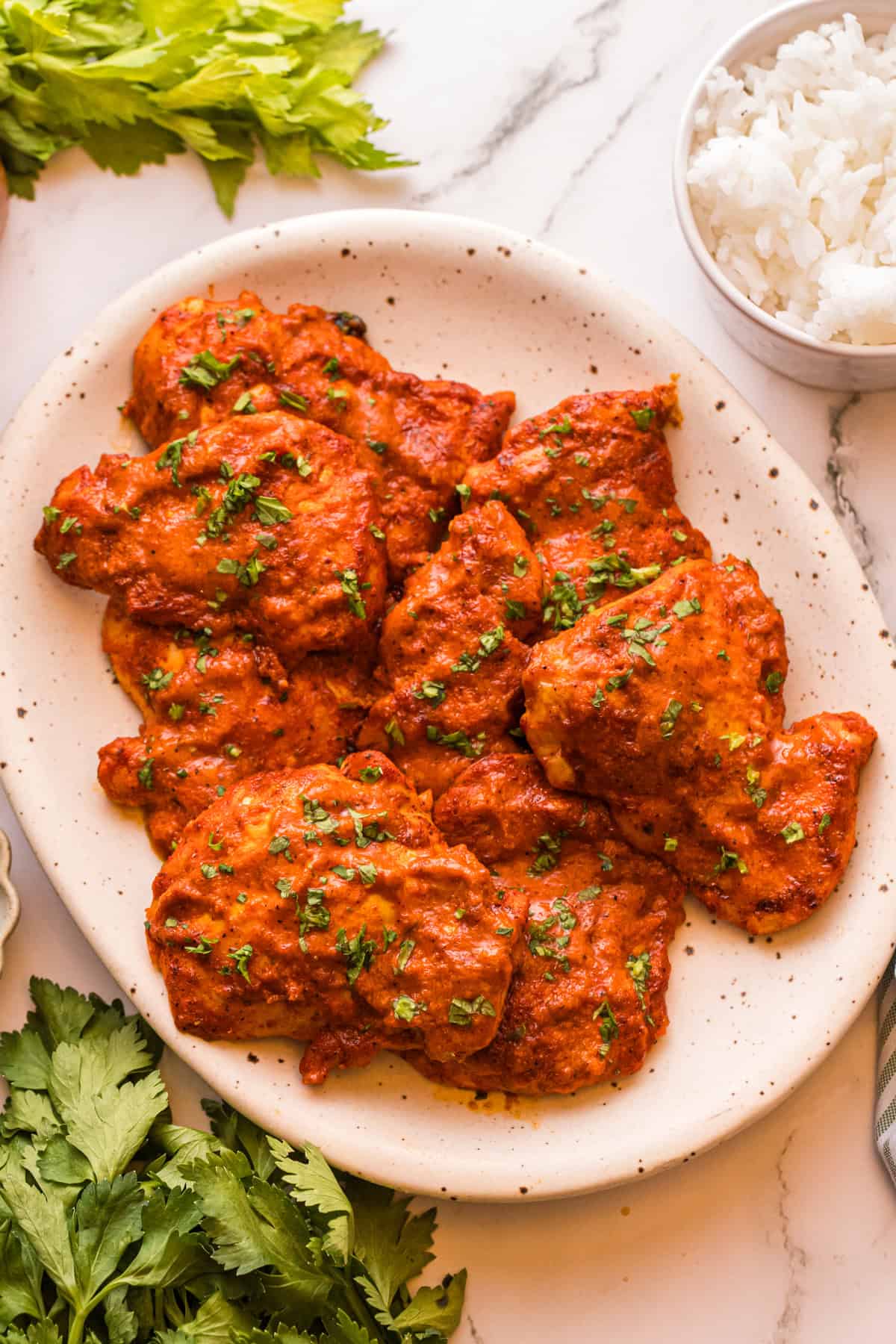 Peri peri chicken thighs on a speckled platter, garnished with chopped parsley, with a bowl of white rice on the side.