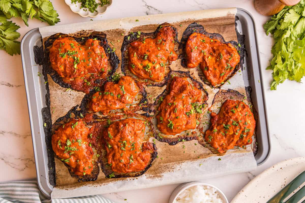 Peri peri chicken thighs brushed with finishing sauce and topped with parsley on a sheet pan.