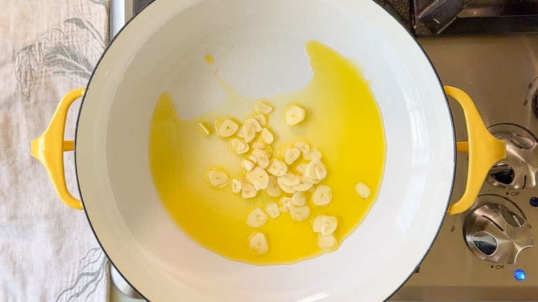 Olive oil and thin garlic slices in Dutch oven on stovetop