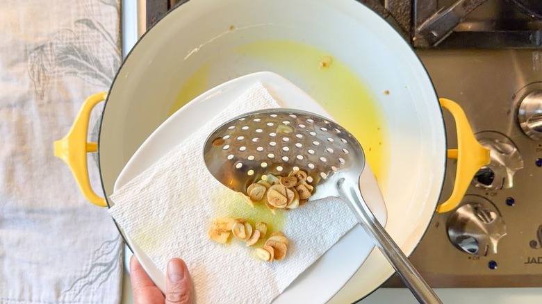 Using a slotted spoon to transfer fried garlic chips from Dutch oven to paper towel-lined plate