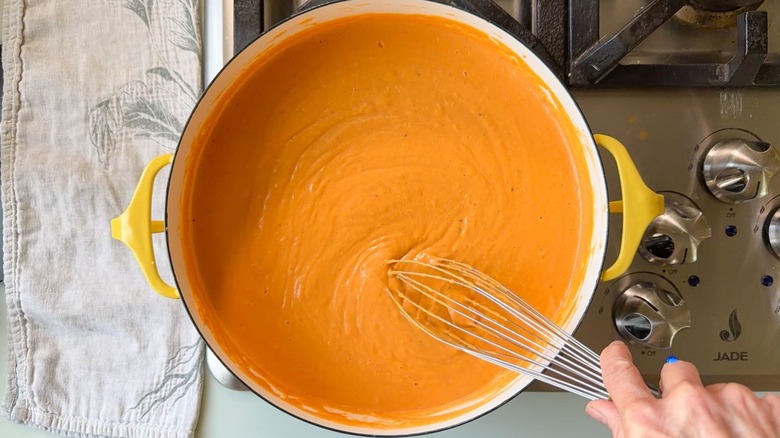 Whisking ultra-creamy white bean tomato soup in Dutch oven on stovetop