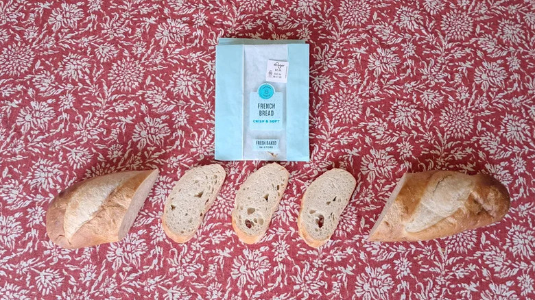 Sliced loaf ofFrench bread against a red and white pattered cloth, with its blue bag sitting above