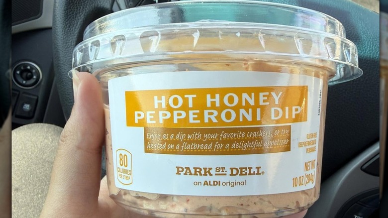 A woman holding a container of Park Street Deli Hot Honey Pepperoni Dip from Aldi