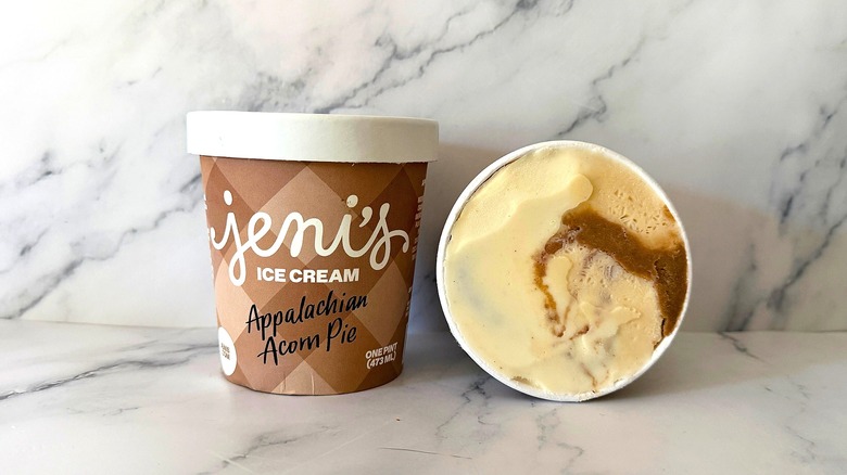 Open container of Jeni's Appalachian Acorn Pie ice cream laying down next to upright pint of ice cream on marble surface