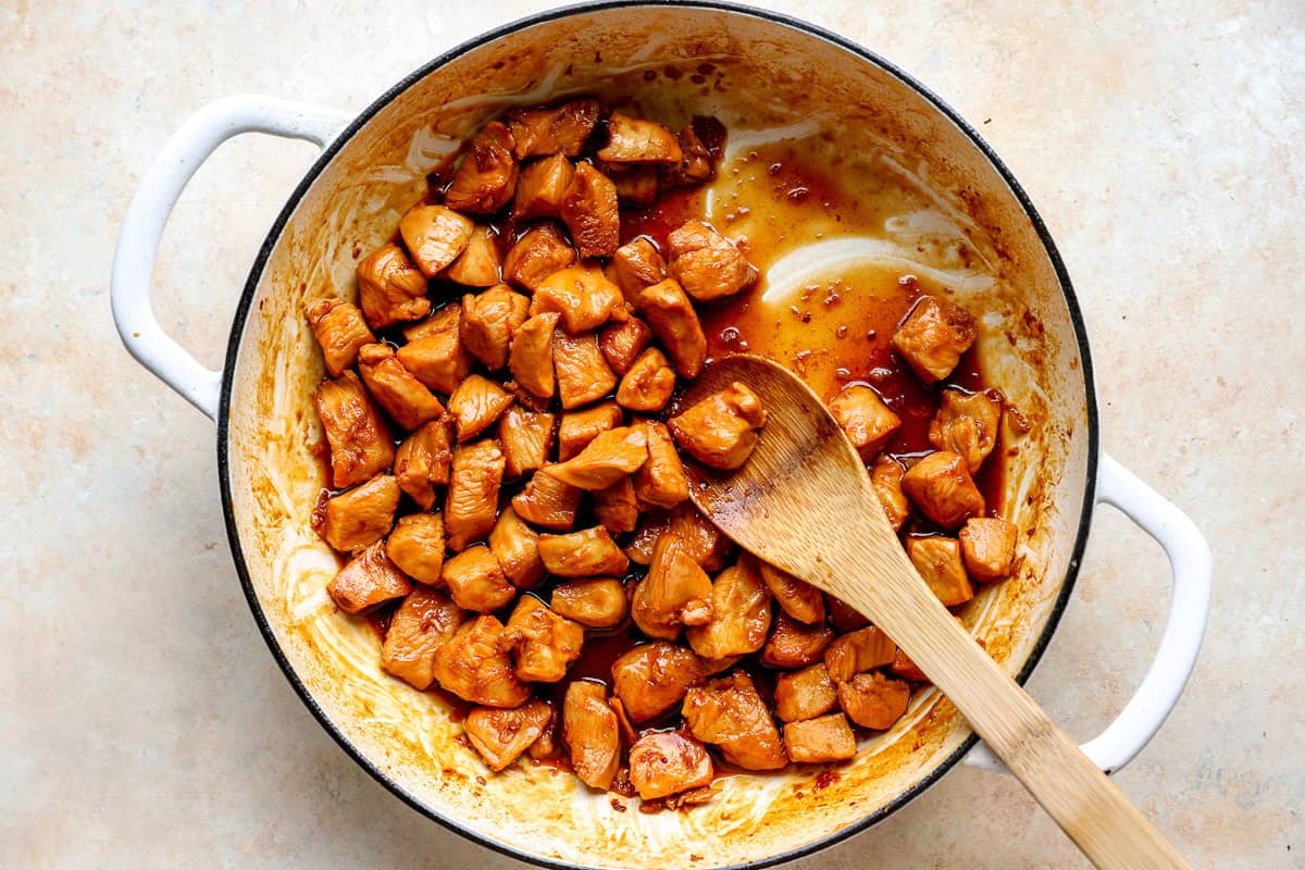Thickened bourbon sauce coating the chicken in a skillet, with a wooden spoon pulled through the sauce.