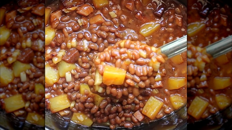 A spoon dishing up beans and pineapple