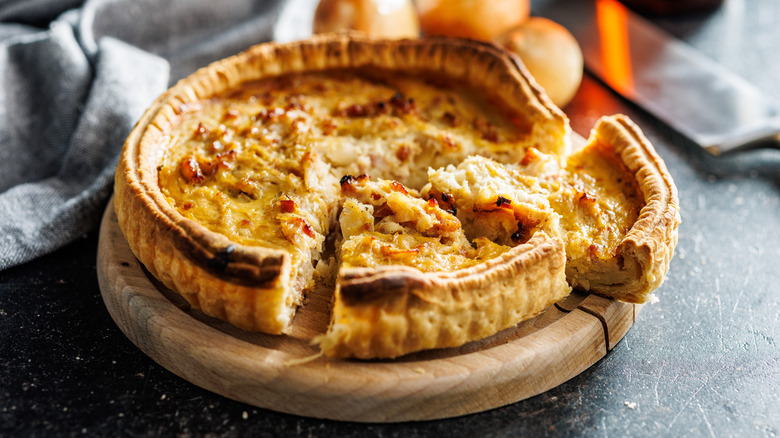 A quiche with two slices separated sits on a wooden board on a black countertop.
