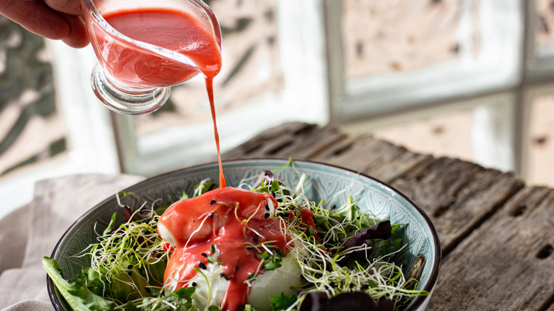 Raspberry vinaigrette being poured onto a salad of greens and sprouts.