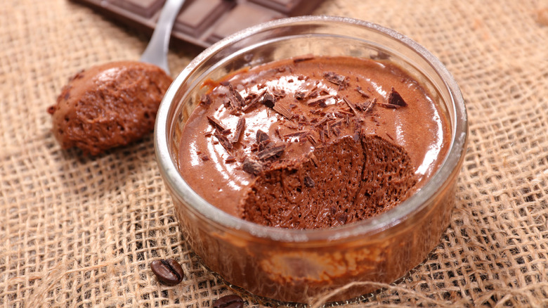 A pot of chocolate mousse sits on burlap with a spoonful of mousse behind it.