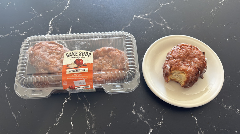 A container of Bake Shop Apple Fritters next to a bitten fritter on a white plate