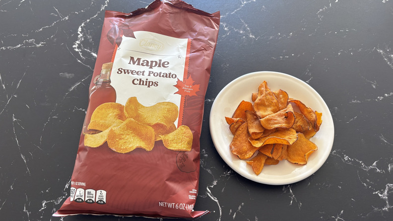 A bag of Clancy's Maple Sweet Potato Chips next to a handful of chips on a white plate