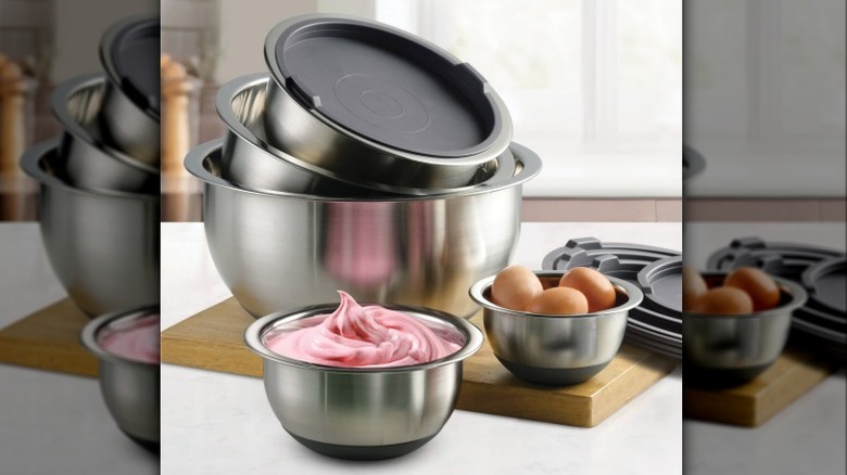 A set of stainless steel mixing bowls with silicone lids displayed on a cutting board